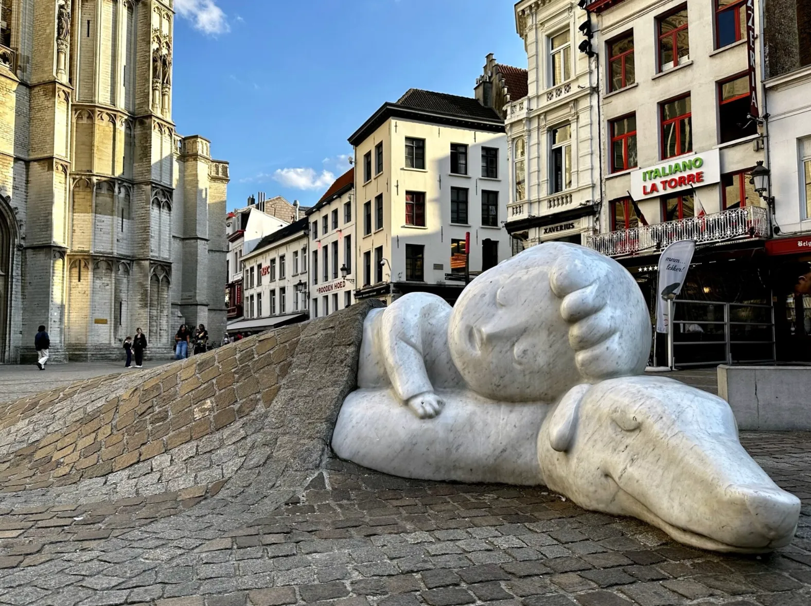 A boy and his dog asleep, carved at ground level under a blanket of cobblestones.