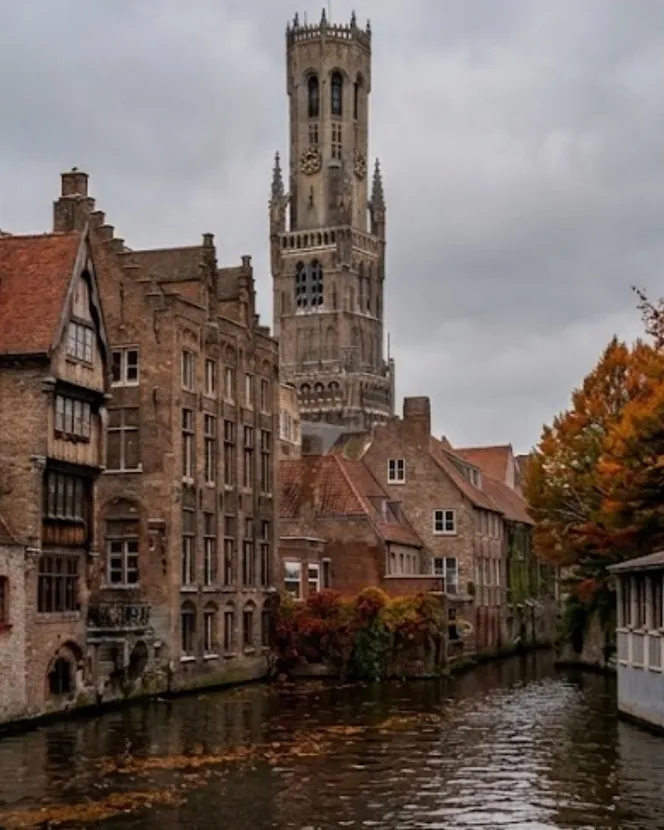 The Rozenhoedkaai in Bruges in autumn: a low grey sky, an orange maple leaning over the canal and fallen leaves drifting on the water.
